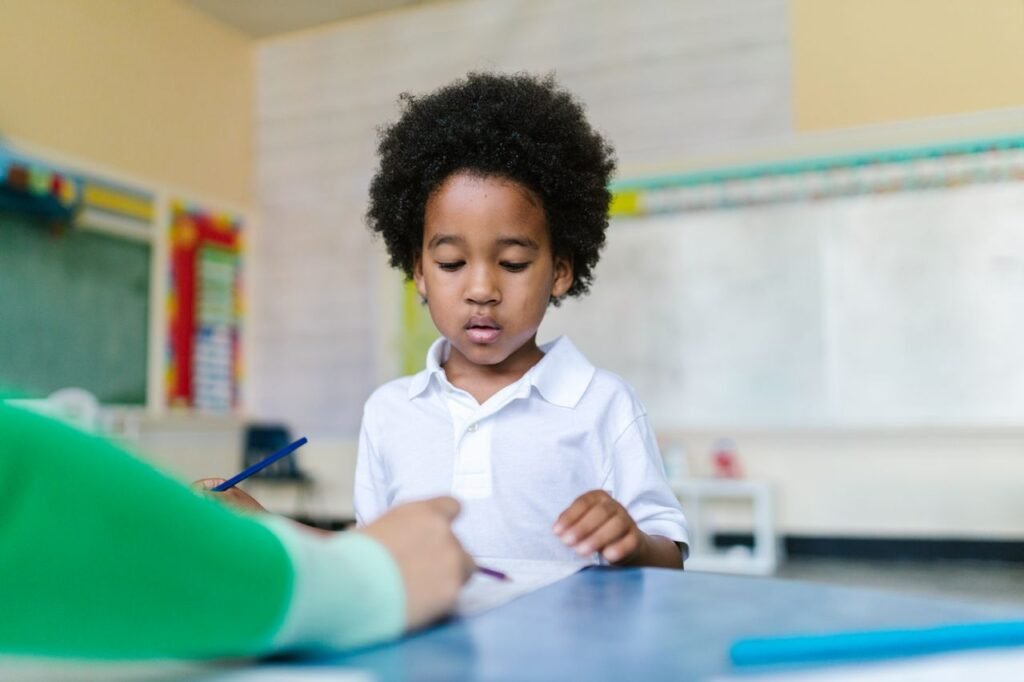 A young boy with afro hair learning in a bright classroom setting, engaged in a task.